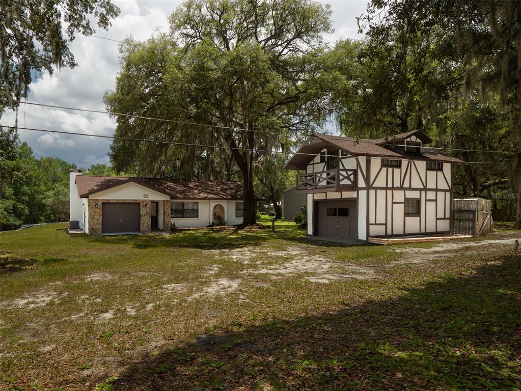 A single-story house with a stone facade and a detached two-story Tudor-style garage building — 121 SERENA CIRCLE, MELROSE, FL