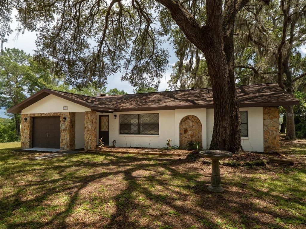 A single-story house with white stucco walls, stone accents, and a brown roof under trees — 121 SERENA CIRCLE, MELROSE, FL