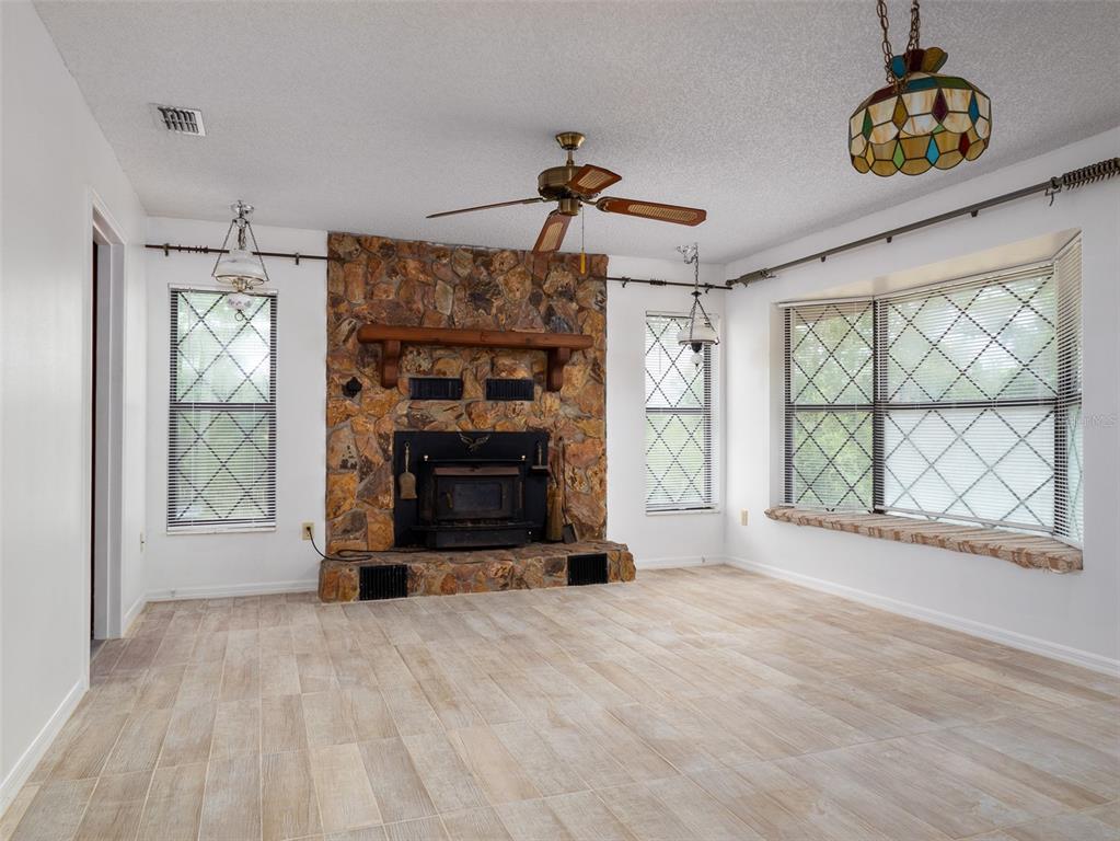 A living room features a stone fireplace, wood-look tile flooring, and a large bay window — 121 SERENA CIRCLE, MELROSE, FL