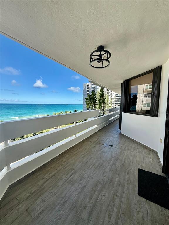 A balcony with wood-look tile flooring overlooks the ocean and a neighboring building — 1510 ASHFORD AVENUE UNIT 7E, SAN JUAN, PR