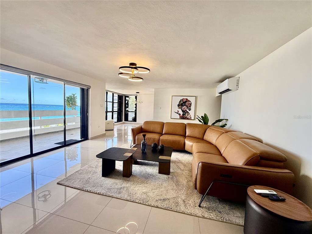 A living room features a tan sectional sofa, a geometric rug, and a balcony overlooking ocean — 1510 ASHFORD AVENUE UNIT 7E, SAN JUAN, PR