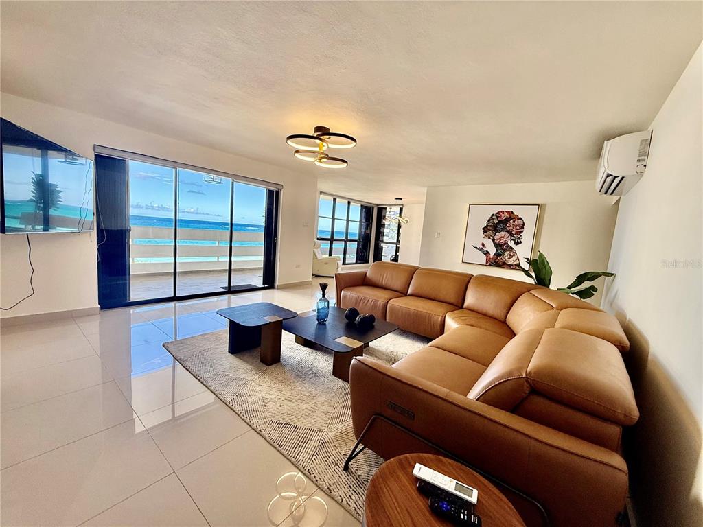 A living room features a large tan sectional sofa, a coffee table, and ocean views — 1510 ASHFORD AVENUE UNIT 7E, SAN JUAN, PR