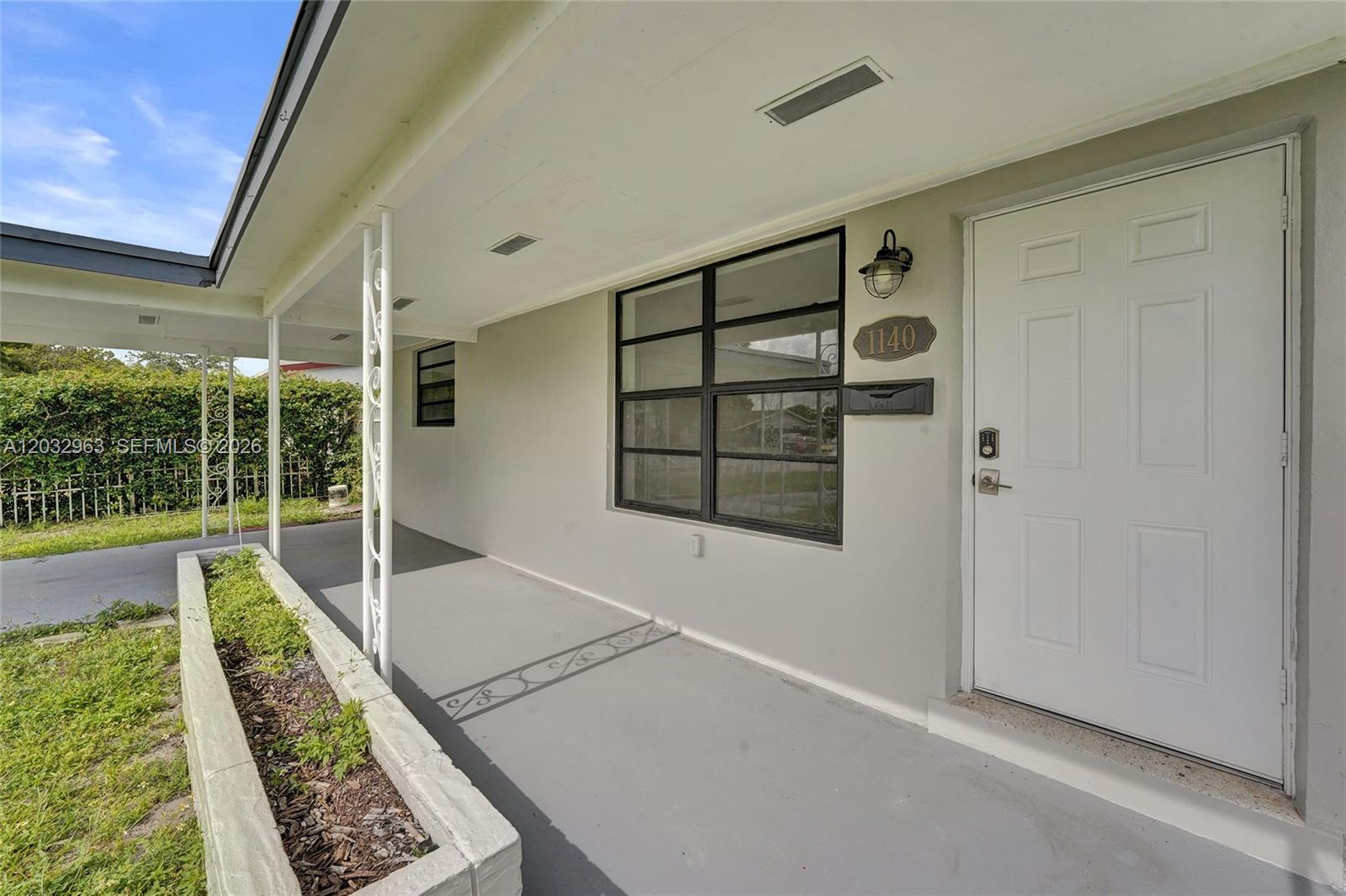 A covered porch features a concrete floor, a white front door, and a planter box — 1140 N 74th Way, Hollywood FL 33024, HOLLYWOOD, FL