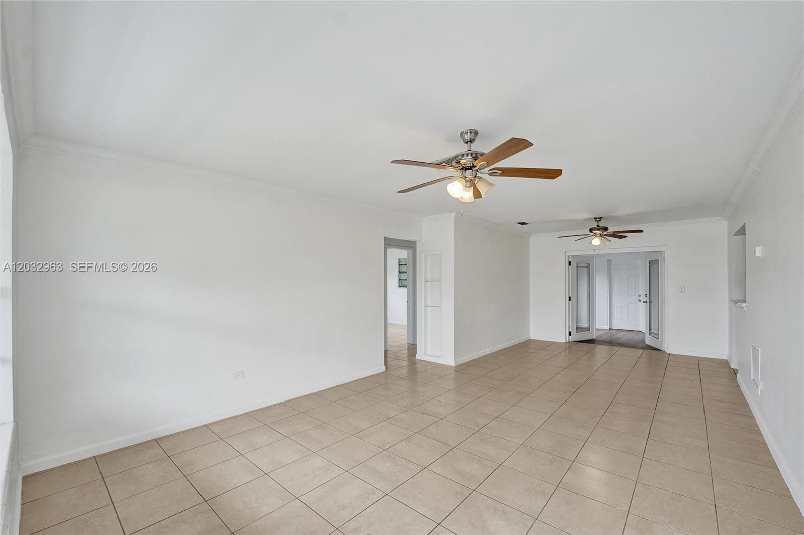 An empty room features white walls, tan tile flooring, and two ceiling fans — 1140 N 74th Way, Hollywood FL 33024, HOLLYWOOD, FL