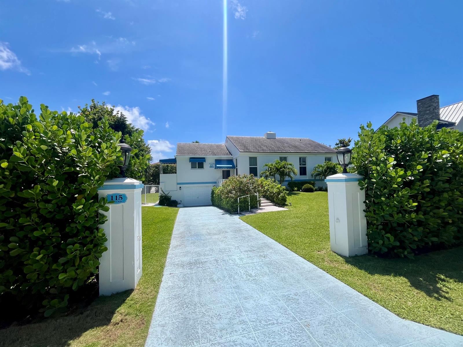 A white house with a blue-tiled driveway and matching blue awnings sits behind two pillars — 115 Dolphin Road, Ocean Ridge FL 33435, OCEAN RIDGE, FL