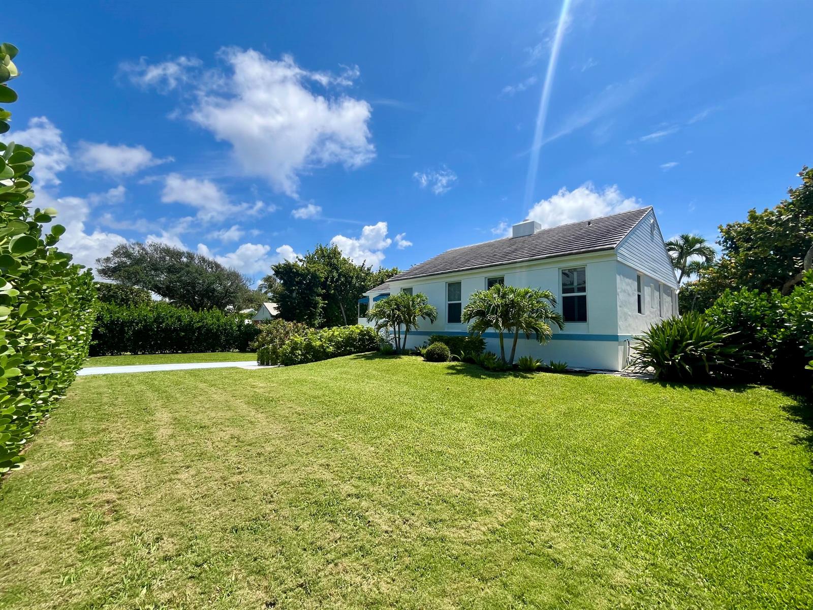 A white house with a blue trim sits on a large, grassy lawn under blue skies — 115 Dolphin Road, Ocean Ridge FL 33435, OCEAN RIDGE, FL