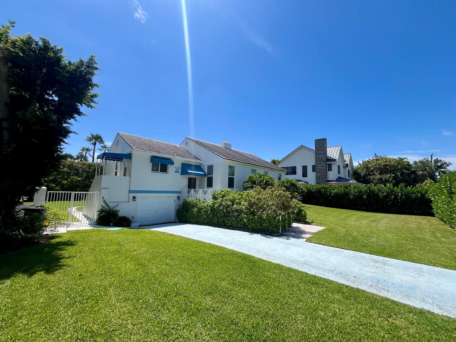 A white house with blue awnings and a garage sits behind a green lawn — 115 Dolphin Road, Ocean Ridge FL 33435, OCEAN RIDGE, FL