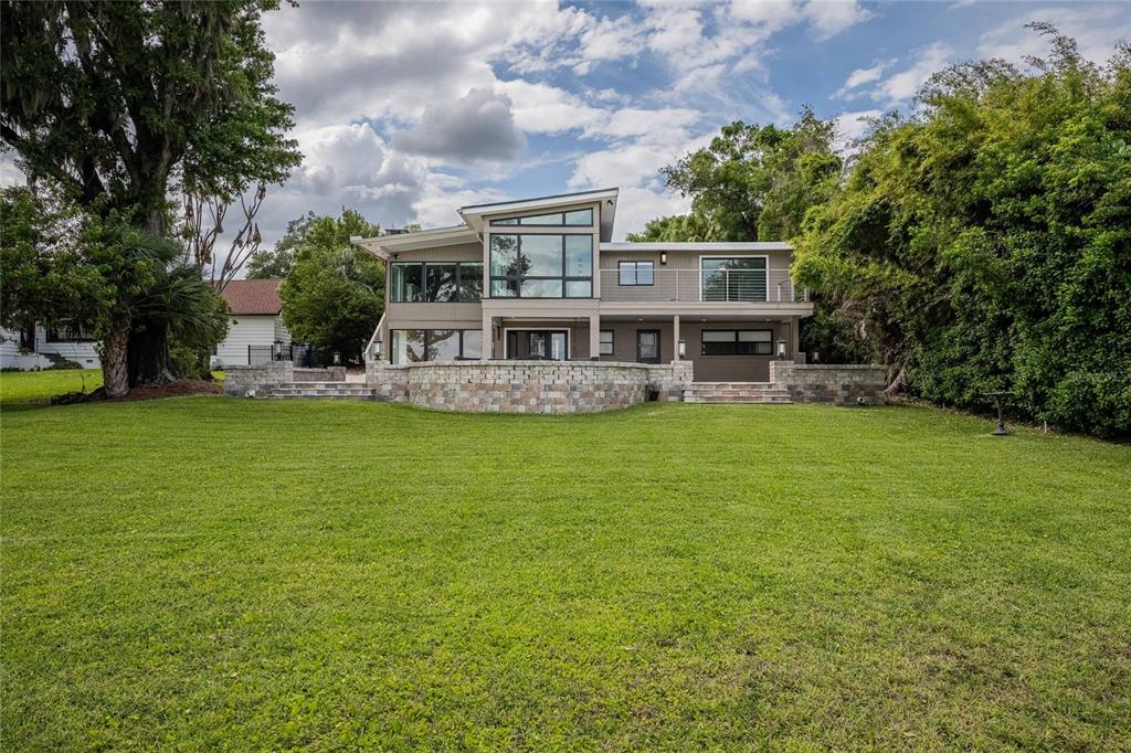 A modern two-story house with a stone retaining wall sits behind a large grassy lawn — 7 LAKE HOLLINGSWORTH DRIVE, LAKELAND, FL