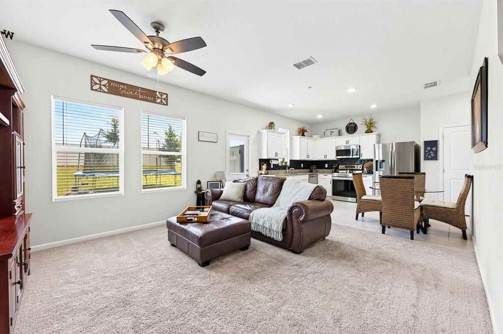 An open-concept living room and kitchen featuring a brown leather sofa, dining area, and windows — 1961 HEMINGWAY CIRCLE, GROVELAND, FL
