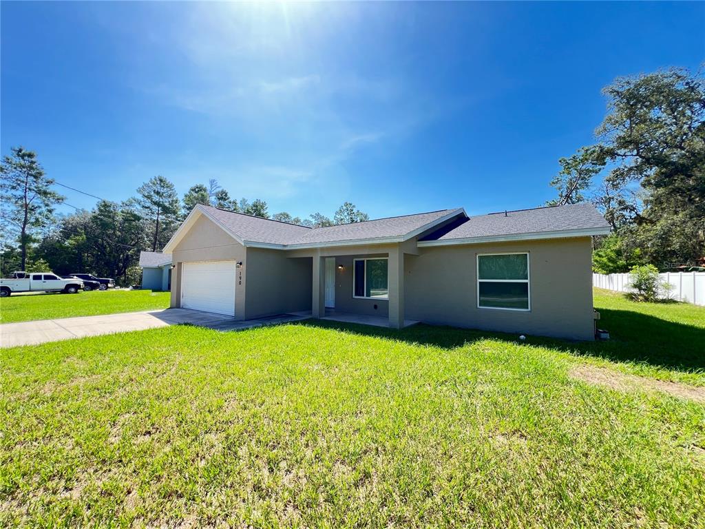 A single-story tan house with a two-car garage and a front porch under a blue sky — 190 FISHER WAY, OCKLAWAHA, FL