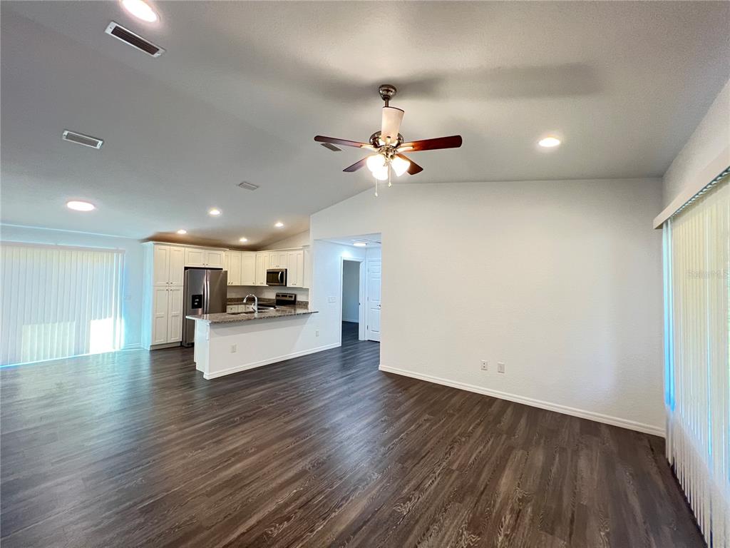 An open-concept living area features dark wood-look flooring, a kitchen with white cabinets, and a ceiling fan — 190 FISHER WAY, OCKLAWAHA, FL