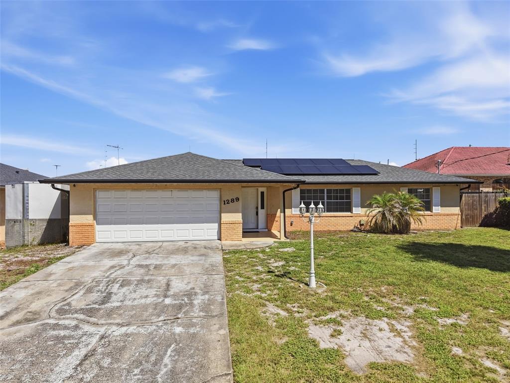A single-story house with a concrete driveway, solar panels, and a brick-accented exterior — 1289 DANDELION DRIVE, DELTONA, FL