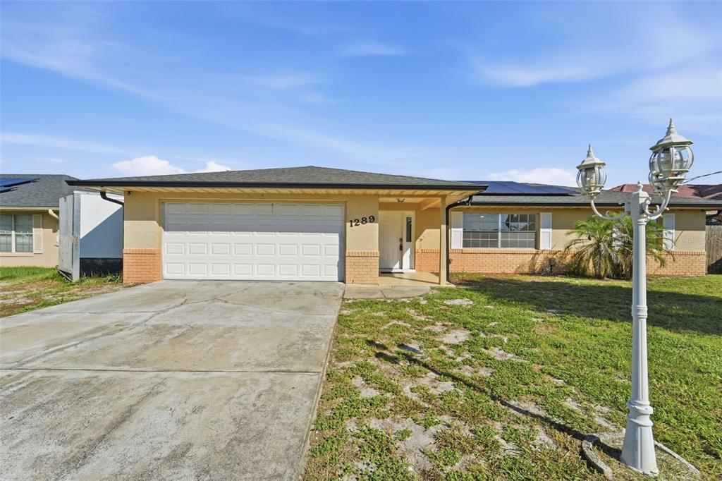 A single-story house with a two-car garage, brick accents, and a front yard lawn — 1289 DANDELION DRIVE, DELTONA, FL
