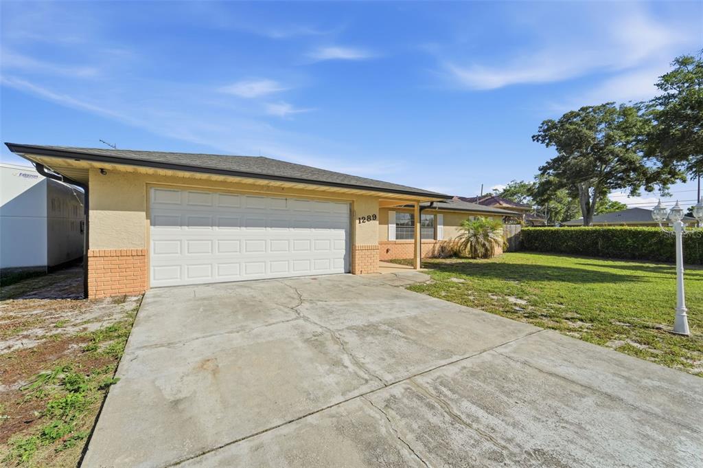 A single-story house with a beige stucco exterior, a two-car garage, and a concrete driveway — 1289 DANDELION DRIVE, DELTONA, FL
