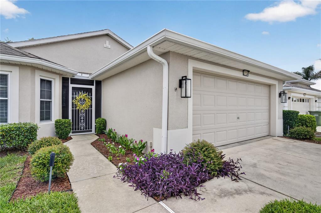 A beige house exterior features a front door with a decorative screen and a garage — 27134 NOSTALGIA DRIVE, LEESBURG, FL
