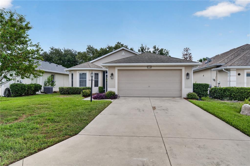 A single-story suburban house with a beige stucco exterior, a two-car garage, and a driveway — 27134 NOSTALGIA DRIVE, LEESBURG, FL