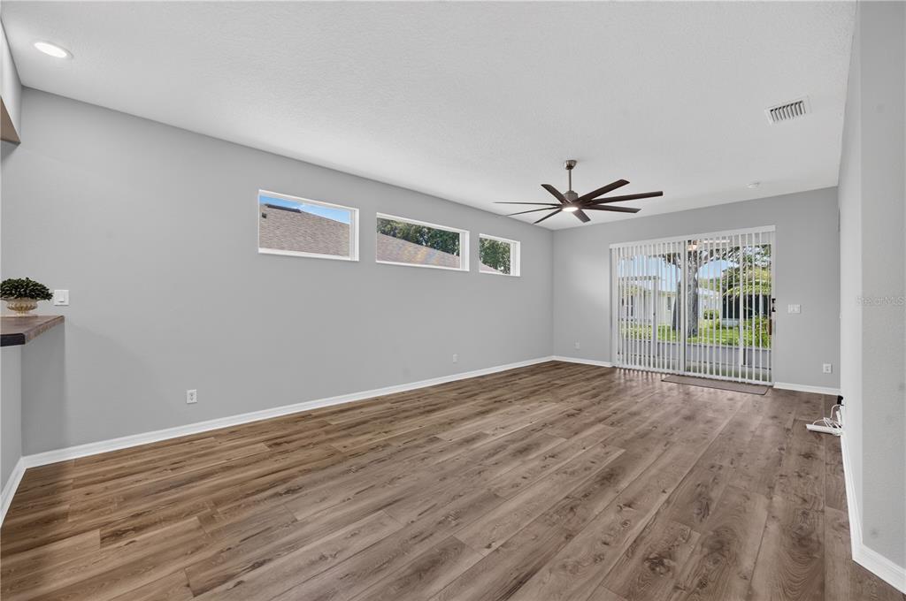 An empty living room features wood-look flooring, gray walls, a ceiling fan, and sliding glass doors — 27134 NOSTALGIA DRIVE, LEESBURG, FL