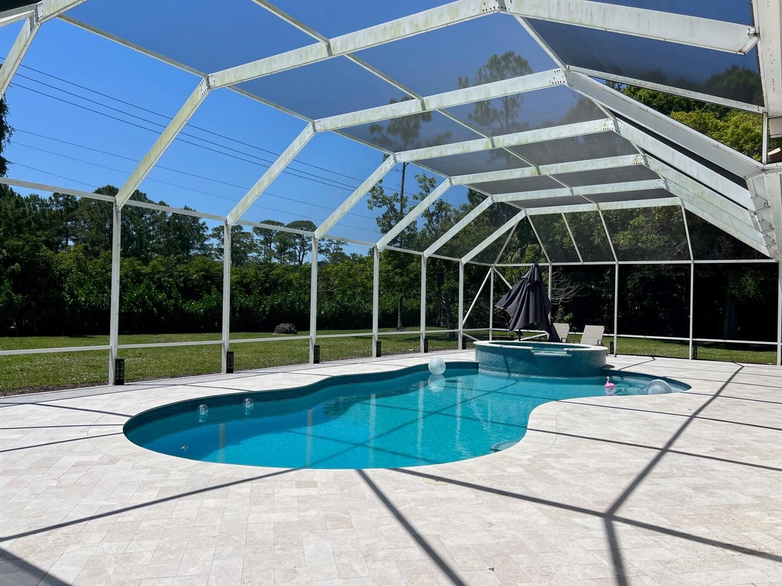 A screened-in swimming pool and spa with a light-colored paver deck under a clear sky — 103 Squire Drive, Wellington FL 33414, WELLINGTON, FL