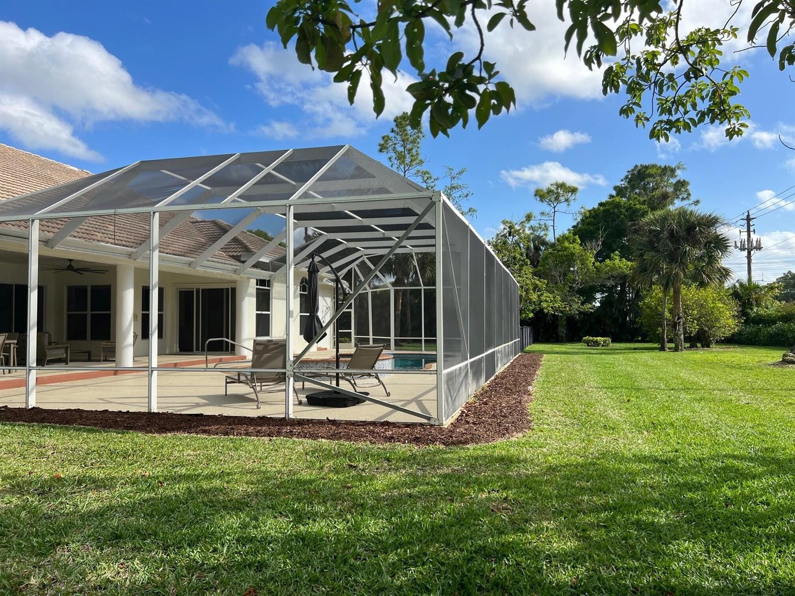 A screened-in pool enclosure sits on a concrete patio next to a grassy backyard — 103 Squire Drive, Wellington FL 33414, WELLINGTON, FL