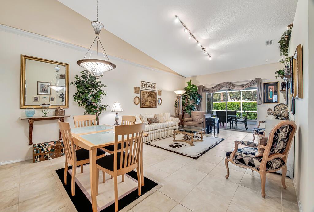 An empty living room features beige tile flooring, a vaulted ceiling, and sliding glass doors — 8482 Logia Circle, Boynton Beach FL 33472, BOYNTON BEACH, FL