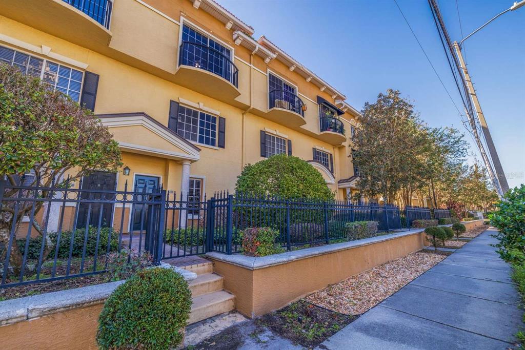 A multi-story yellow townhouse exterior with black balconies, a metal fence, and a sidewalk — 5252 W KENNEDY BOULEVARD, TAMPA, FL