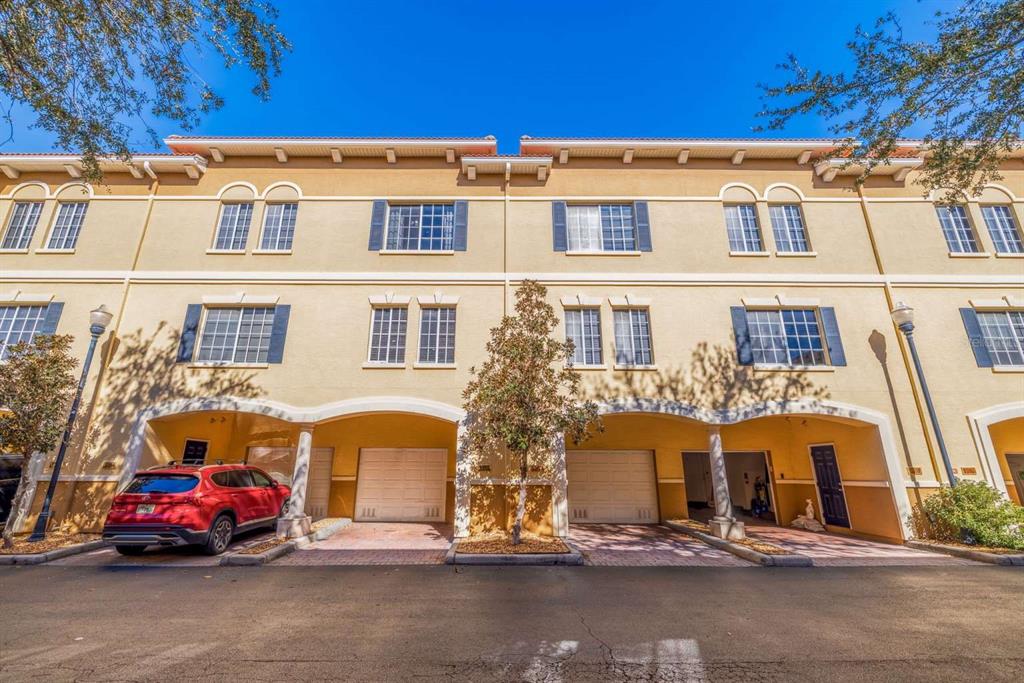 A three-story townhouse exterior features tan stucco walls, arched garage openings, and a red car — 5252 W KENNEDY BOULEVARD, TAMPA, FL