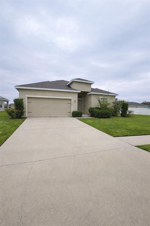 A single-story house with a beige stucco exterior, a two-car garage, and a concrete driveway — 446 GLENKIRK WAY, LAKE ALFRED, FL