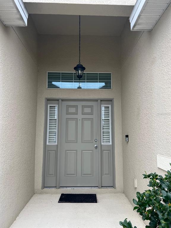 A gray front door with sidelights and a transom window under a covered entryway — 446 GLENKIRK WAY, LAKE ALFRED, FL