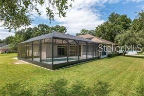 A backyard view of a house with a screened-in pool enclosure and a grassy lawn — 5060 SE 40TH STREET, OCALA, FL