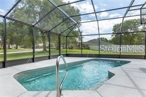 A screened-in swimming pool with a metal handrail sits on a concrete patio — 5060 SE 40TH STREET, OCALA, FL