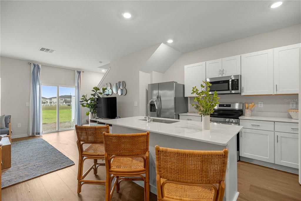 A kitchen with white cabinets and a center island overlooks a living area with sliding doors — 4968 SW 83RD PLACE, OCALA, FL