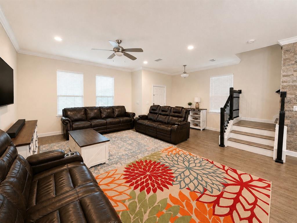 A living room features dark leather sofas, a colorful floral rug, and a staircase — 10253 LOVE STORY STREET, WINTER GARDEN, FL