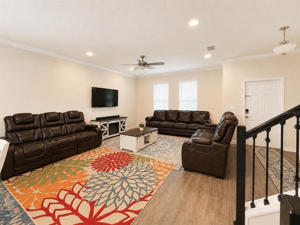 A living room features dark leather furniture, a patterned area rug, and wood-look flooring — 10253 LOVE STORY STREET, WINTER GARDEN, FL