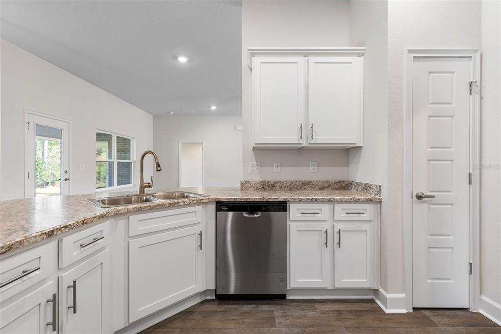 A kitchen features white cabinets, granite countertops, a stainless steel dishwasher, and a sink — 36 RYMSHAW DRIVE, PALM COAST, FL