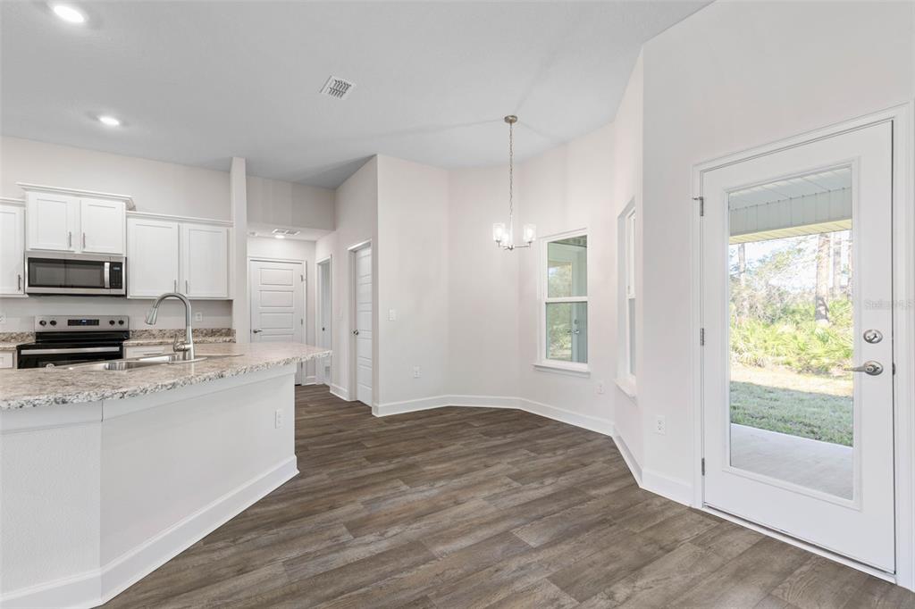 A kitchen with white cabinets and granite countertops opens to a dining area with wood-look flooring — 36 RYMSHAW DRIVE, PALM COAST, FL