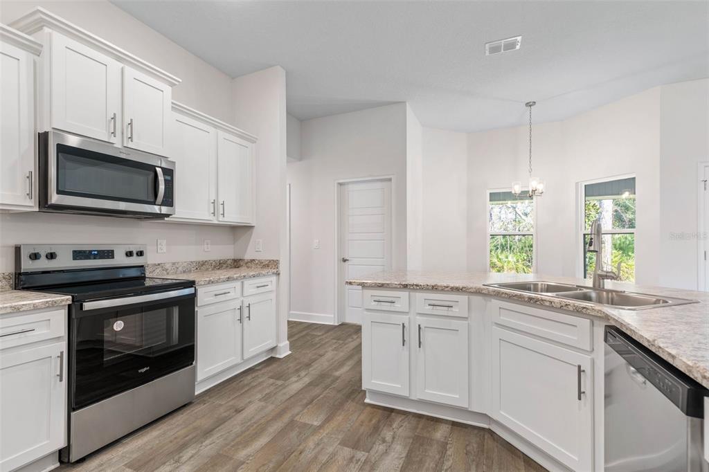 A kitchen with white cabinets, stainless steel appliances, granite countertops, and wood-look flooring — 36 RYMSHAW DRIVE, PALM COAST, FL