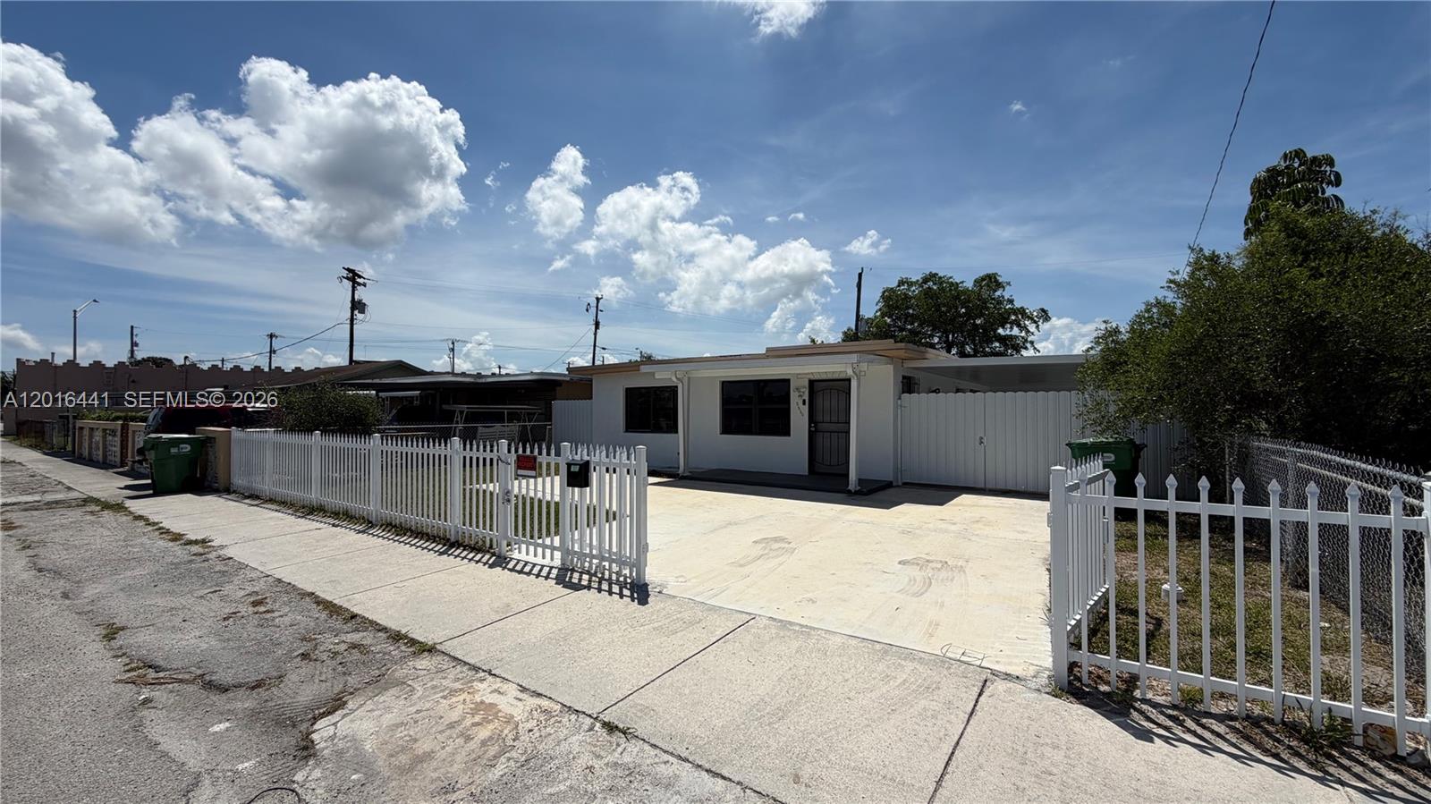 A single-story house with a white fence and a concrete driveway under a blue sky — 2230 Service Rd, Opa-Locka FL 33054, OPA-LOCKA, FL