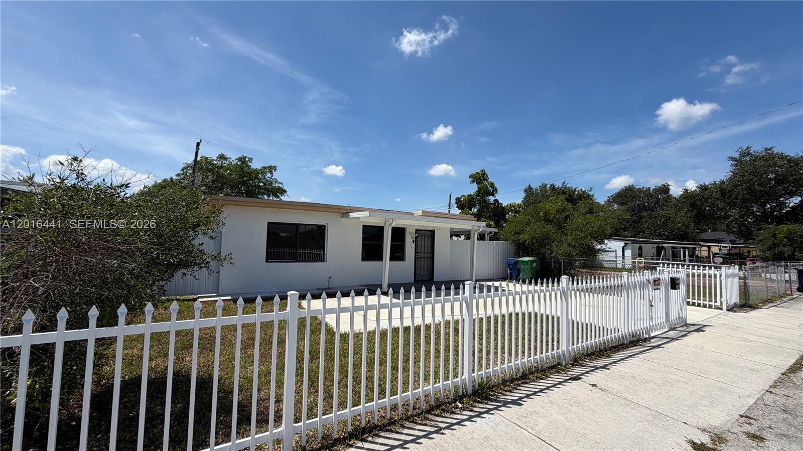 A white single-story house with a white picket fence and a paved front yard — 2230 Service Rd, Opa-Locka FL 33054, OPA-LOCKA, FL