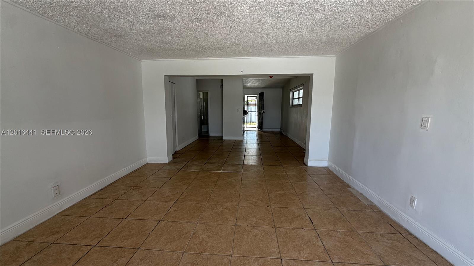 An empty room with tan floor tiles and white walls leads to an exterior doorway — 2230 Service Rd, Opa-Locka FL 33054, OPA-LOCKA, FL
