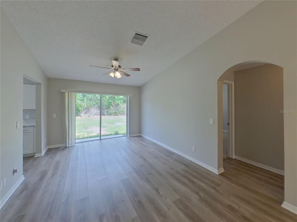An empty living room features light wood-look flooring, a ceiling fan, and sliding glass doors — 13346 PRESTWICK DRIVE, RIVERVIEW, FL