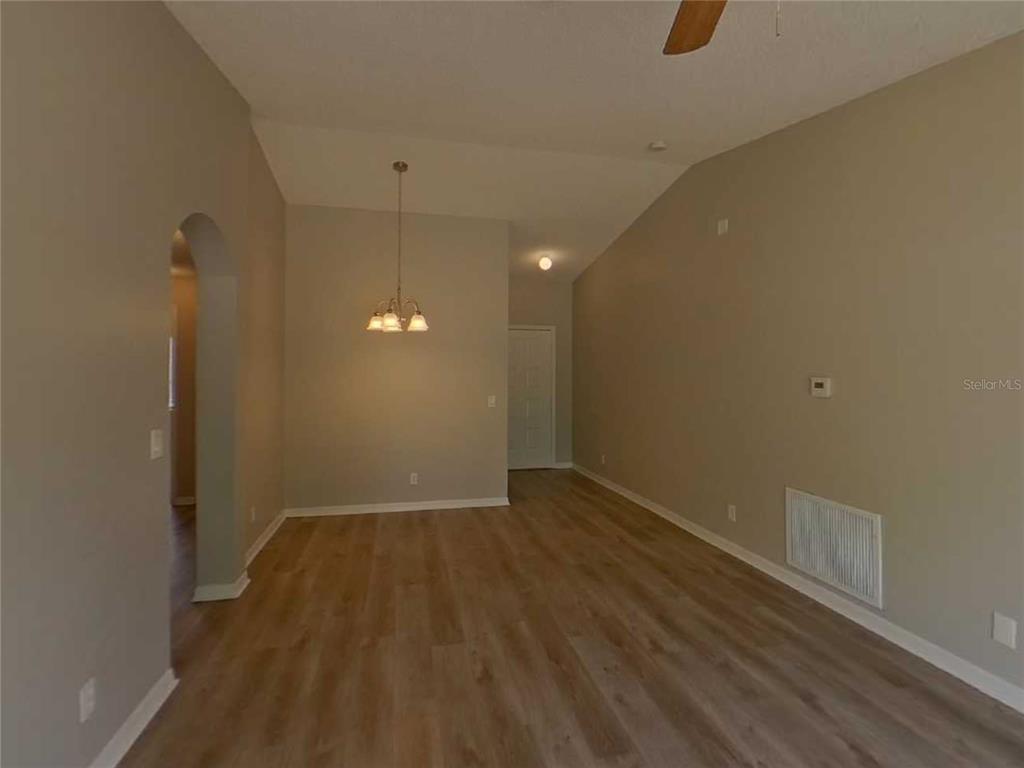 An empty room with light wood-look flooring, a vaulted ceiling, and a hanging light fixture — 13346 PRESTWICK DRIVE, RIVERVIEW, FL