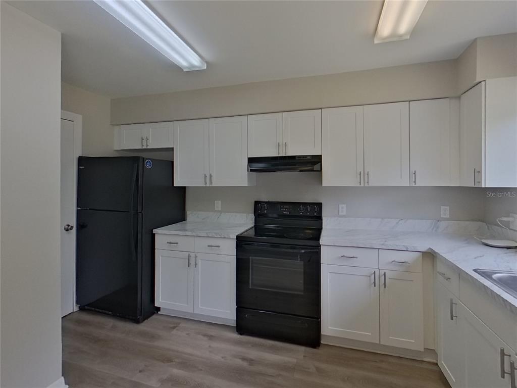 A kitchen features white cabinets, black appliances, and marble-look countertops over wood-style flooring — 13346 PRESTWICK DRIVE, RIVERVIEW, FL