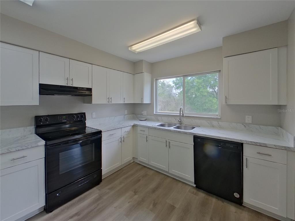 A kitchen features white cabinets, black appliances, marble-look countertops, and light wood-look flooring — 13346 PRESTWICK DRIVE, RIVERVIEW, FL