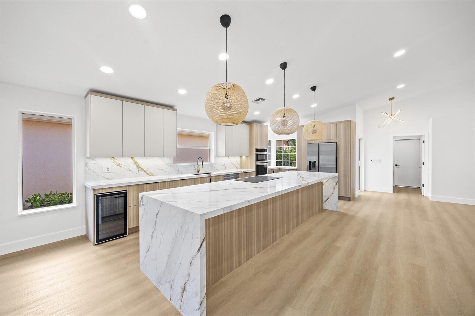 An open-concept kitchen, dining, and living area featuring light wood cabinetry and marble countertops — 5141 Columbo Court, Delray Beach FL 33484, DELRAY BEACH, FL