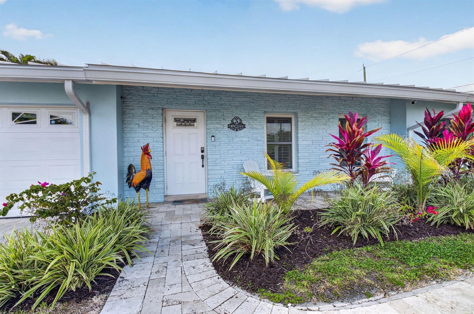 A light blue brick house features a white front door, a rooster statue, and landscaping — 5800 NE 7th Avenue, Boca Raton FL 33487, BOCA RATON, FL