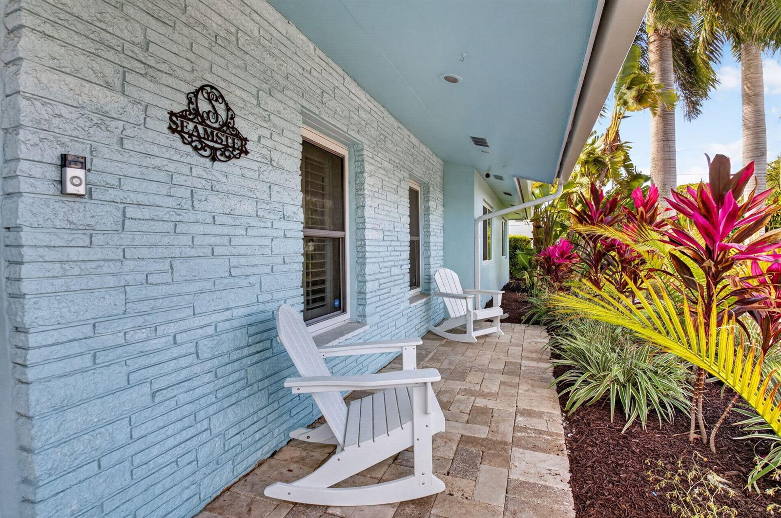 A light blue brick house exterior features a stone patio with two white rocking chairs — 5800 NE 7th Avenue, Boca Raton FL 33487, BOCA RATON, FL