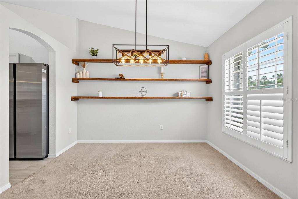 A dining area features three wooden floating shelves, a rectangular chandelier, and carpeted flooring — 4394 CUTHBERT AVENUE, NORTH PORT, FL