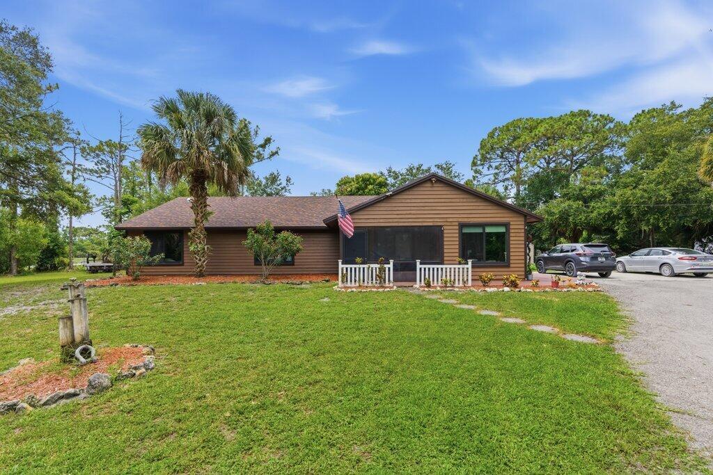A single-story brown house with a screened porch and an American flag stands on grass — 16888 Hialeah Drive W, FL 33470, FL