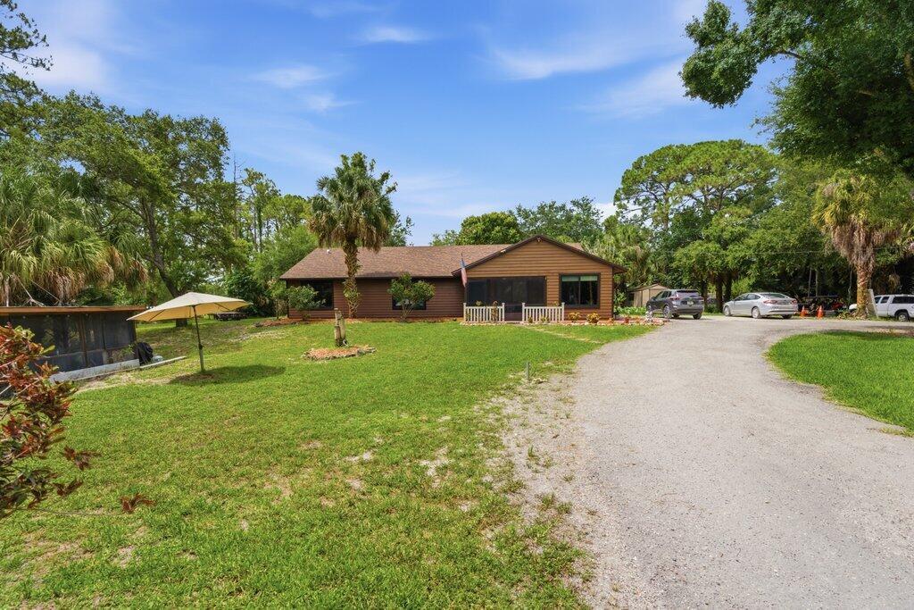A single-story brown house with a gravel driveway and a large grassy yard — 16888 Hialeah Drive W, FL 33470, FL