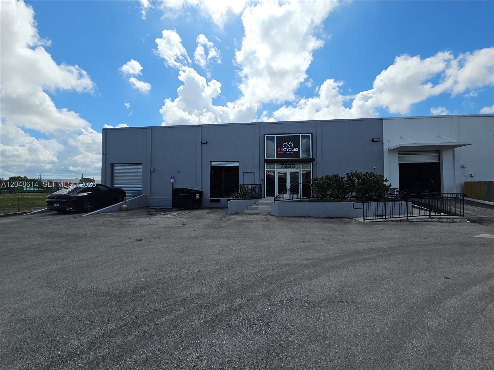 The exterior of a gray commercial warehouse building features a storefront entrance and loading bays — 7890 NW 34th St, Doral FL 33122, DORAL, FL